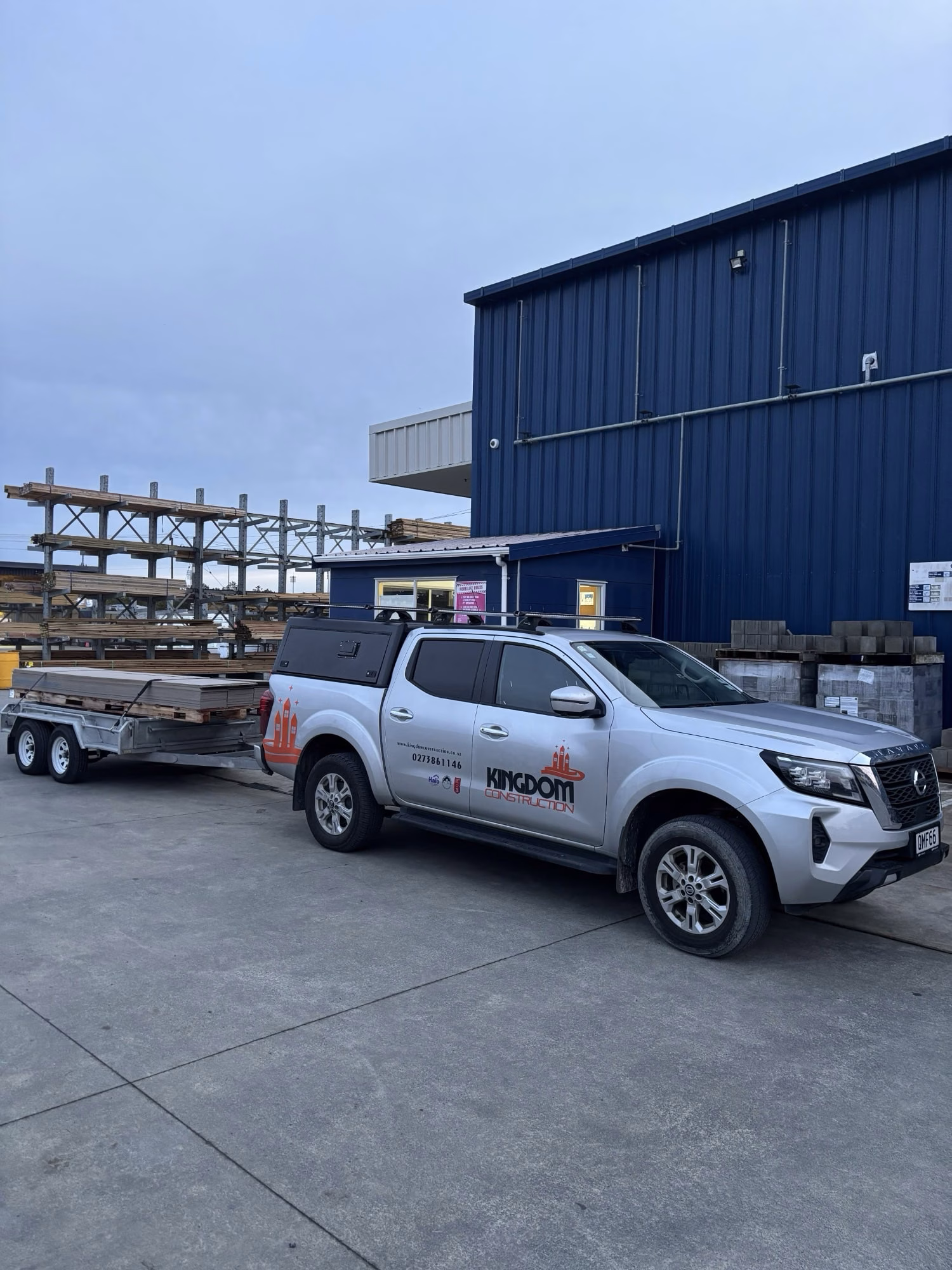 Kingdom Construction branded ute towing a trailer loaded with timber at a building supplies yard