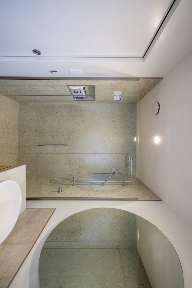 Modern bathroom with stone-tiled shower area, fold-down shower seat, overhead rain shower, and arched alcove below