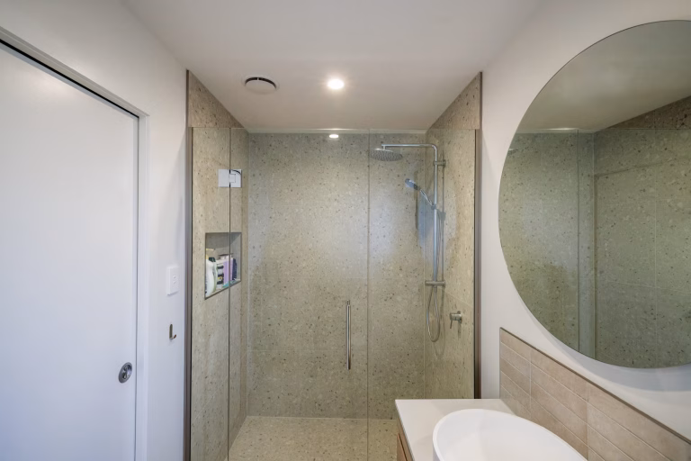 Modern bathroom with stone-tiled shower area, fold-down shower seat, overhead rain shower, and arched alcove below